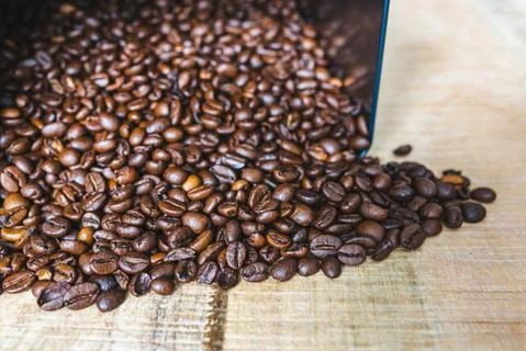 Roasted brown coffee beans inside square tin can spilled on wooden background Stock Photos
