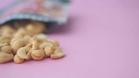 Roasted cashew nuts spilled from packaging bag onto pink background in cine.. Stock Footage 332141209