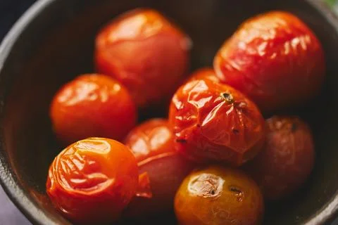 Roasted cherry Tomatoes placed in a ceramic dark bowl. Close up macro shot. Stock Photos