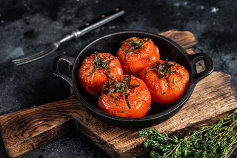 Roasted cherry tomatoes with thyme in a pan. Black background. Top view Stock Photos