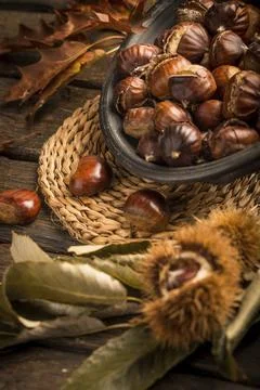 Roasted chestnuts on a rustic wooden table with autumn leaves in the background Stock Photos