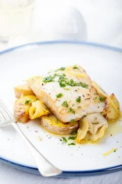 Roasted cod, codfish with baked potatoes and artichokes with lemon and herb.. Stock Photos