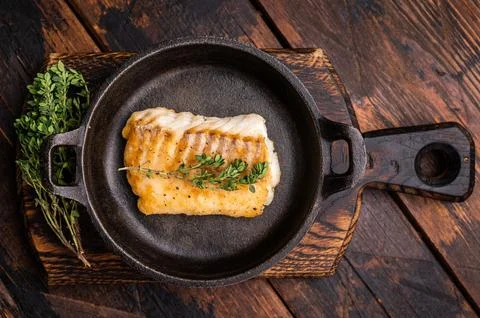 Roasted cod fish loin fiilet in skillet. Wooden background. top view Stock Photos