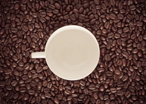Roasted coffee bean background with white ceramic mug in the middle. Stock Photos