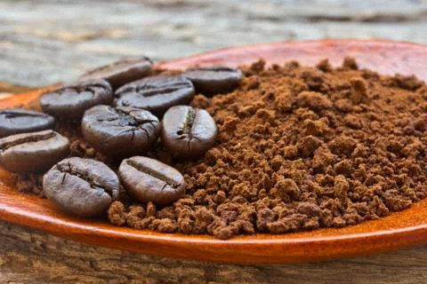 Roasted coffee beans and ground coffee in wooden spoon on textured wood. Stock Photos