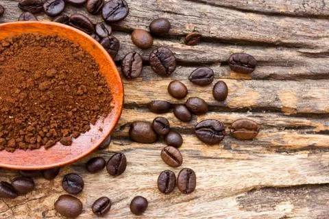 Roasted coffee beans and ground coffee in wooden spoon on textured wood. Stock Photos
