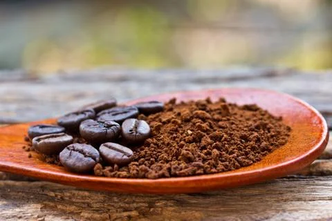 Roasted coffee beans and ground coffee in wooden spoon on textured wood. Stock Photos