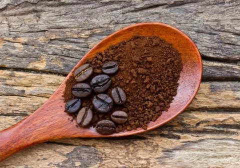 Roasted coffee beans and ground coffee in wooden spoon on textured wood. Stock Photos