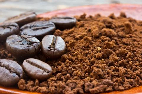 Roasted coffee beans and ground coffee in wooden spoon on textured wood. Stock Photos