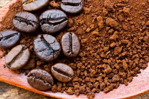 Roasted coffee beans and ground coffee in wooden spoon on textured wood. Stock Photos