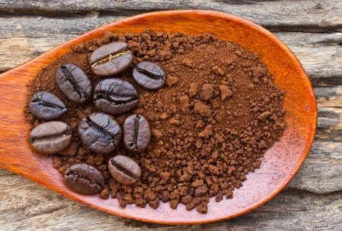 Roasted coffee beans and ground coffee in wooden spoon on textured wood. Stock Photos
