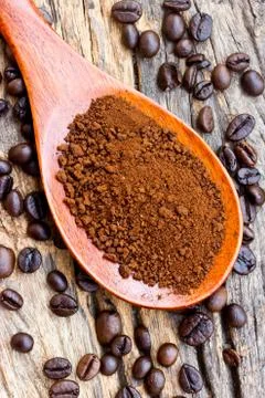 Roasted coffee beans and ground coffee in wooden spoon on textured wood. Stock Photos