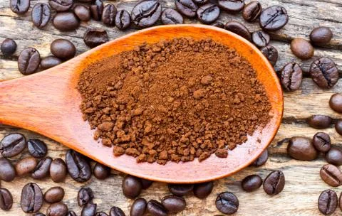 Roasted coffee beans and ground coffee in wooden spoon on textured wood. Stock Photos