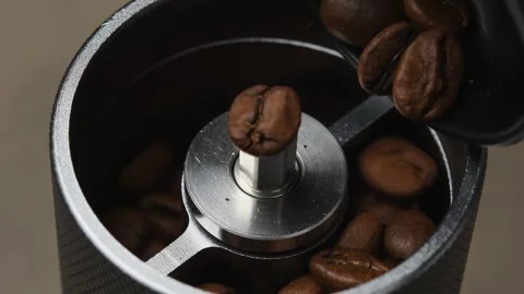 Roasted coffee beans are poured by hand into a manual coffee grinder during Stock Footage 346743808