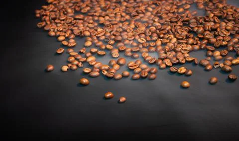 Roasted coffee beans on a black background with steam . Stock Photos