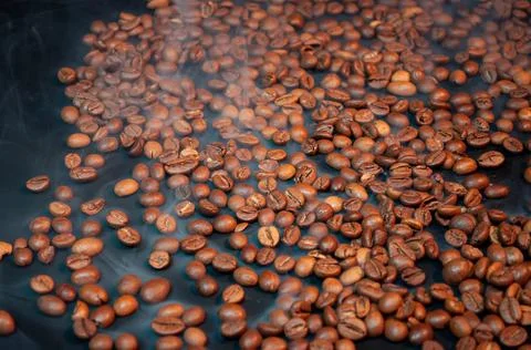 Roasted coffee beans on a black background with steam . Stock Photos