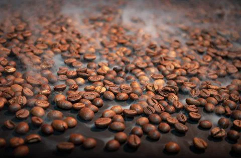 Roasted coffee beans on a black background with steam . Stock Photos