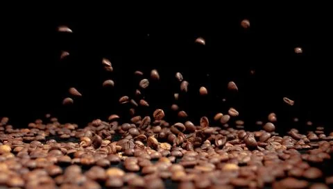 Roasted coffee beans on a black background in the process of falling . Stock Photos
