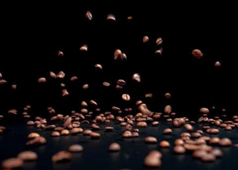 Roasted coffee beans on a black background in the process of falling . Stock Photos