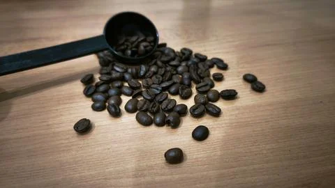 Roasted Coffee Beans with Black Measuring Scoop on Wooden Table Photos