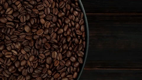 Roasted coffee beans in black plate rotating top view. dark wooden background Video stock 131512926