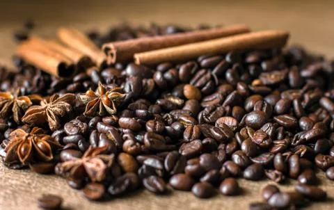 Roasted coffee beans in bulk on a table with cinnamon and star anise. . Dark Stock Photos