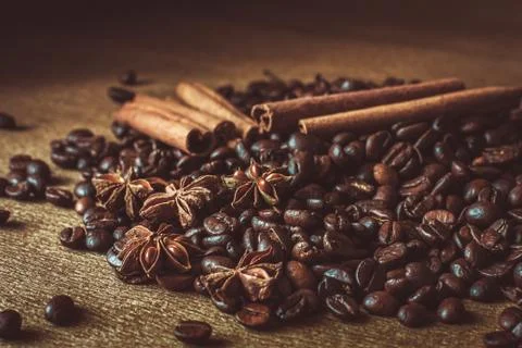 Roasted coffee beans in bulk on a table with cinnamon and star anise. . Dark Stock Photos