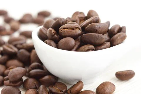Roasted coffee beans in ceramic measuring scoop. On fabric. Stock Photos