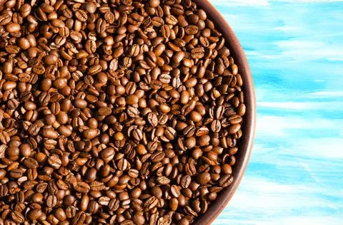 Roasted coffee beans in a ceramic plate on a turquoise background. Stock Photos