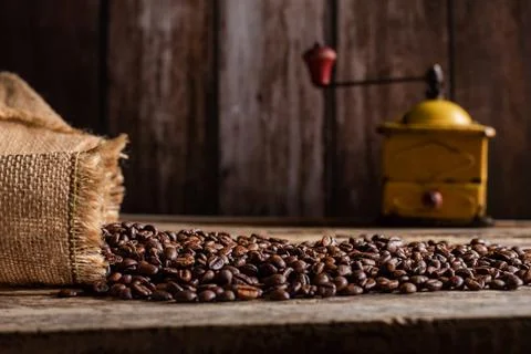 Roasted coffee beans coming out of a sack on a wooden table and in the back.. Stock Photos