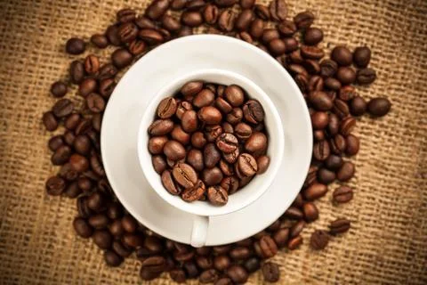 Roasted coffee beans in a cup on burlap background Stock Photos