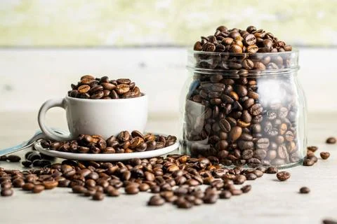 Roasted coffee beans in cup Roasted coffee beans in cup and in jar on whit... Stock Photos