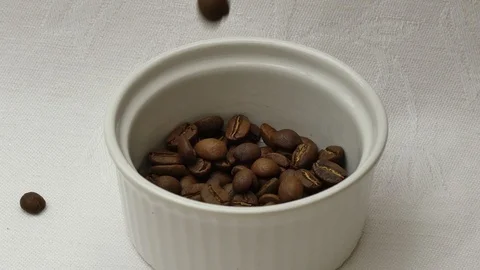 Roasted Coffee beans fall into small white bowl, spilling over Stock Footage 125474004