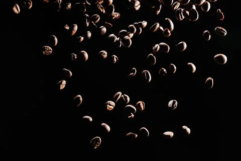 Roasted coffee beans falling against black background Stock Photos