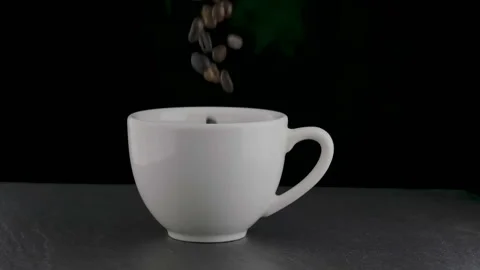 Roasted coffee beans falling down into white coffee cup Video stock 142676496