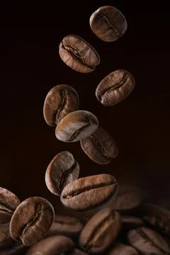 Roasted coffee beans falling on pile. Dark colors Stock Photos