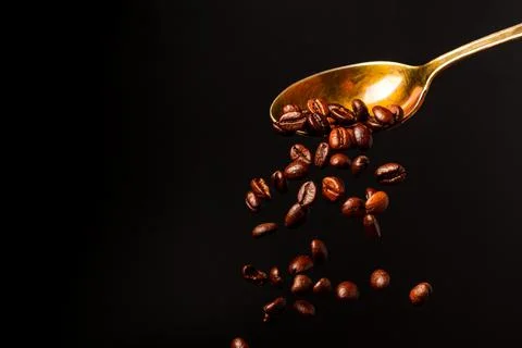 Roasted coffee beans falling from a spoon on a black background. Stock Photos
