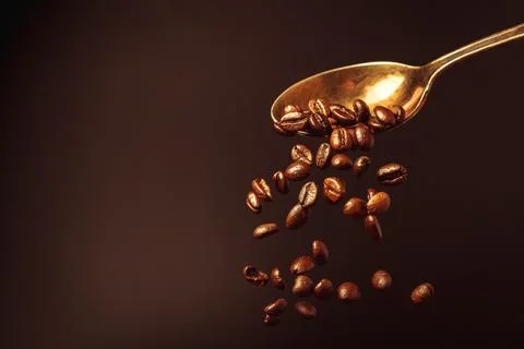 Roasted coffee beans falling from a spoon on a brown background. Stock Photos