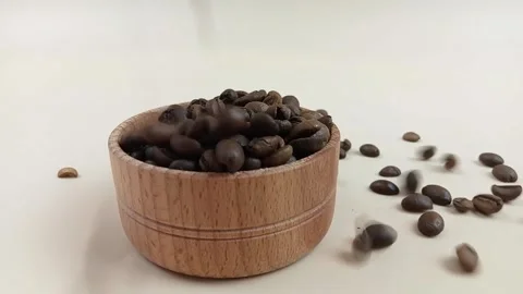 Roasted coffee beans falling into wooden bowl on light background Stock Footage 335144288