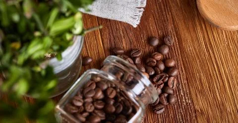 Roasted coffee beans get out of overturned glass jar on wooden background Stock Photos