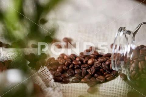 Roasted coffee beans get out of overturned glass jar on homespun tablecloth Stock Photos