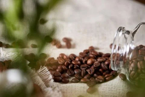 Roasted coffee beans get out of overturned glass jar on homespun tablecloth Stock Photos