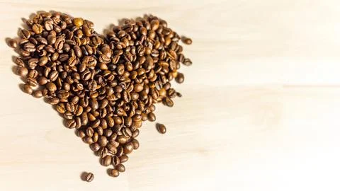Roasted coffee beans in heart shape on light wooden background Stock-Fotos
