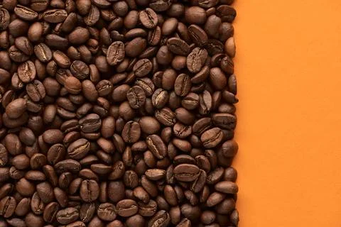 Roasted coffee beans on orange background with copy space. Close up top view. Stock Photos