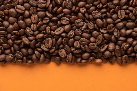 Roasted coffee beans on orange background with copy space. Close up top view. Stock Photos