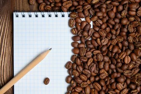 Roasted coffee beans with paper notepad and pencil. Top view. Stock Photos
