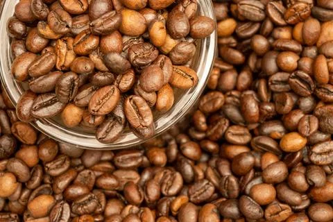 Roasted coffee beans scattered on the table and a small coffee cup. Stock Photos