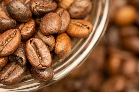 Roasted coffee beans scattered on the table and a small coffee cup. Stock Photos