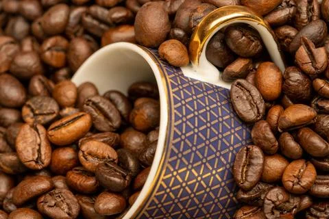 Roasted coffee beans scattered on the table and a small coffee cup. Stock Photos