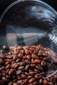 Roasted coffee beans scattered from a tilted glass create. 스톡 사진